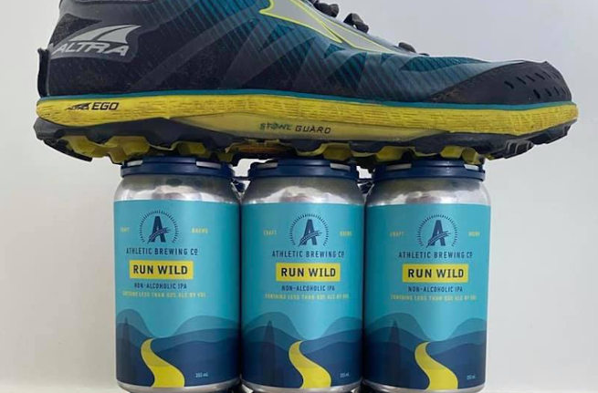 A running shoe on top of a six-pack of Athletic Brewing beers.
