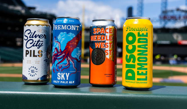 four cans of beer sitting on a rail at a baseball park