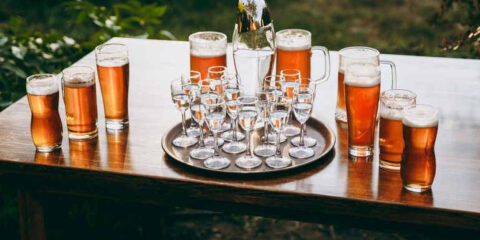 A rustic outdoor wedding beer bar setup featuring a wooden table with a variety of beer glasses and pitchers