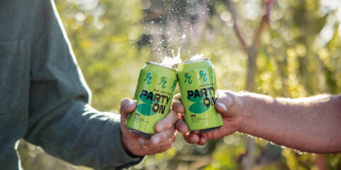 Two hands cheersing with cans of NA beer from Reuben's Brews