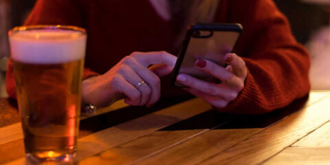 A smartphone-using beer lover sitting at a bar table and playing slots on her smartphone.