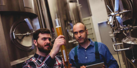 10 Tech Projects Breweries Should Outsource To Save Time And Boost Efficiency Brewers examining beer samples and controlling the brewing operations.