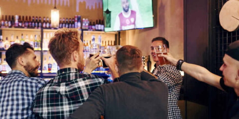 A group of friends having a good time drinking beer and watching a live athletic event on TV in a contemporary beer bar.