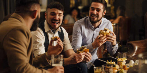 How Local Beer And Restaurant Brands Grow Without Losing Their Soul A group of men is chatting while drinking beers and eating hamburgers at a restaurant