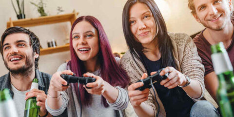 Friends enjoying craft beverages while playing online video games together in a relaxed home setting.