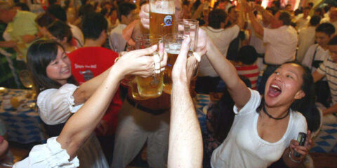Friends drinking together in a spirited mood at a large beer festival with beer mugs raised.