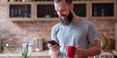 Morning habit, a man holding a coffee cup and a mobile in the kitchen.