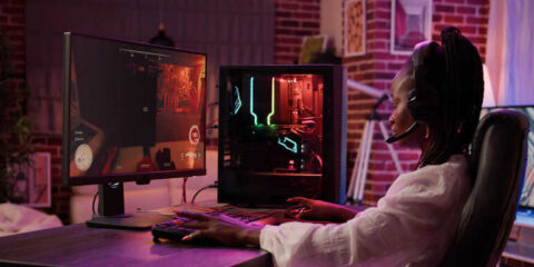 African American gamer girl playing online case battle game on RGB gaming PC setup at home.