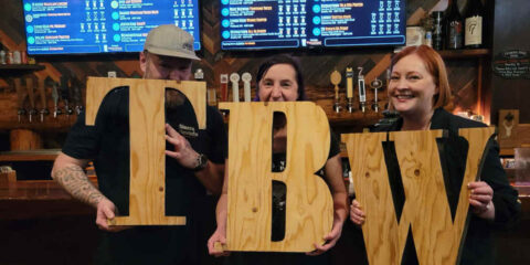 Three people holding a Tacoma Beer Week sign.