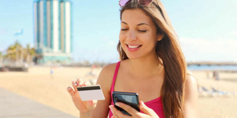 From Street Brews To Beaches: The Best eSIM Data Plans To Support Your Thailand Adventure Traveler using smartphone on beach, enjoying seamless connectivity with eSIM data plan.