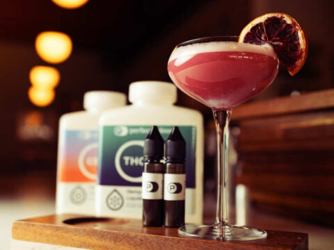 A pink cocktail sitting next to some hemp-derived thc and cbd emulsions.