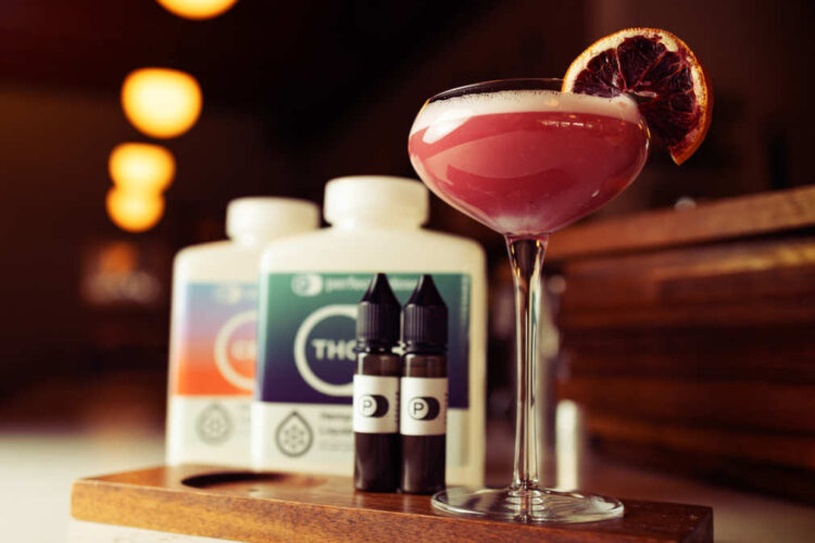 A pink cocktail sitting next to some hemp-derived thc and cbd emulsions.