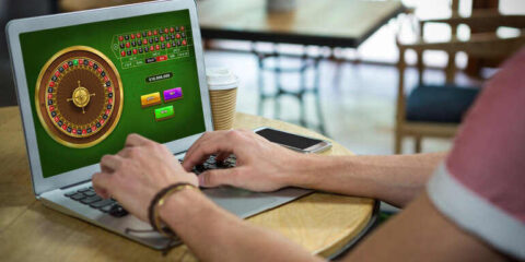 A person plays a digital casino game on a laptop at a cafe table, illustrating a casual and friendly approach to online gaming.