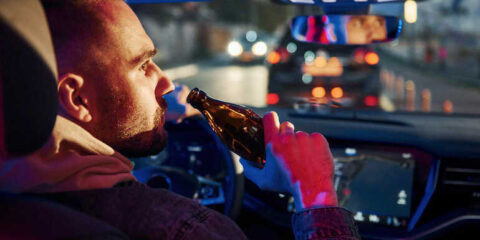 Man in driver’s seat drinking beer while driving at night, highlighting self-driving car alcohol laws in Washington.
