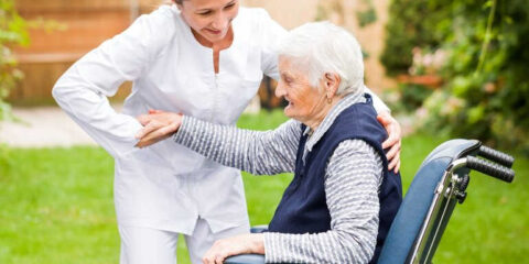Senior caregiver assisting an elderly woman in a wheelchair outdoors, offering support, companionship, and mobility help beyond basic home care.