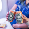 Two cans of beer being held by people on an airplane