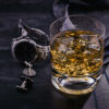 Glass of Scotch whisky with ice on a dark table beside a watch and tie.