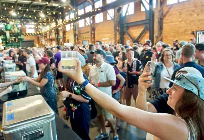 A person raising a glass of beer at a beer festival with a large crowd in the background