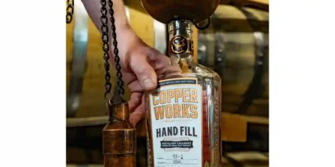 A person hand-filling a whiskey bottle
