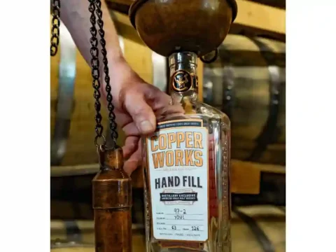 A person hand-filling a whiskey bottle