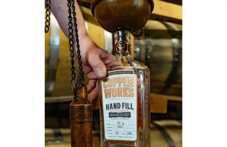 A person hand-filling a whiskey bottle