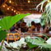 Cozy brewery taproom in Bangkok with patrons enjoying craft beer, warm lighting, and a relaxed indoor atmosphere surrounded by greenery.