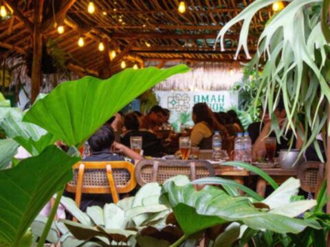 Cozy brewery taproom in Bangkok with patrons enjoying craft beer, warm lighting, and a relaxed indoor atmosphere surrounded by greenery.