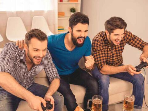 Three friends enjoying a relaxed beer while playing video games together at home.