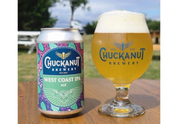 Chuckanut Brewery Colors Outside the Lines and Introduces a West Coast IPA A can of beer next to a glass of beer, sitting on a table outside with grass and trees in the background