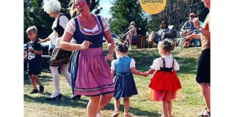 A woman in a dirndl dancing with children at an Oktoberfest celebration