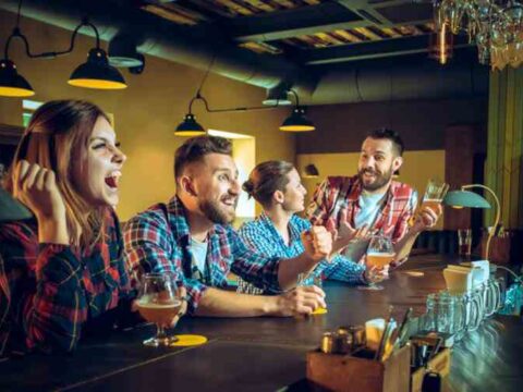 The Rise of Casual Gaming in Bars, Breweries, and Taprooms A group of friends gathered at a lively bar and taproom, laughing and cheering as they enjoyed drinks and casual games in a warm, social atmosphere.