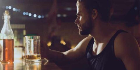 What Does a Healthy Relationship With Alcohol Actually Look Like? A man sits alone at a dimly lit bar, looking thoughtfully at a glass of alcohol.