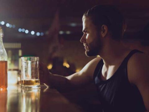 What Does a Healthy Relationship With Alcohol Actually Look Like? A man sits alone at a dimly lit bar, looking thoughtfully at a glass of alcohol.