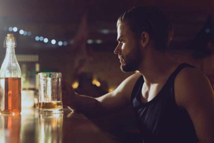 What Does a Healthy Relationship With Alcohol Actually Look Like? A man sits alone at a dimly lit bar, looking thoughtfully at a glass of alcohol.