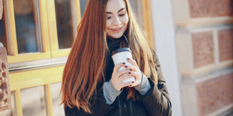 We All Need a Reliable Excuse to Leave the House A smiling woman holding a takeaway coffee outdoors, suggesting a simple reason to step outside on a cold day.