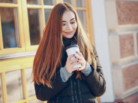 We All Need a Reliable Excuse to Leave the House A smiling woman holding a takeaway coffee outdoors, suggesting a simple reason to step outside on a cold day.