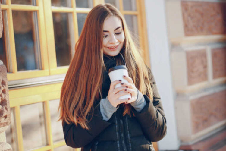 We All Need a Reliable Excuse to Leave the House A smiling woman holding a takeaway coffee outdoors, suggesting a simple reason to step outside on a cold day.