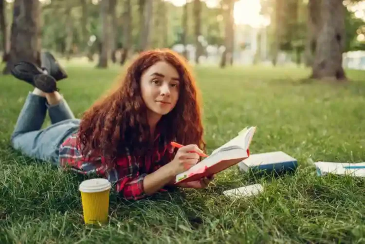How College Students Can Balance Studying, Hobbies, And Social Life Without Burning Out College student girl relaxing in a garden with a book while balancing study, hobbies, and social life.