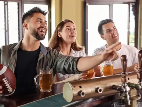 What Is a Parlay Bet: A Beer Lover’s Game Day Guide Friends enjoying beer and watching football at a sports bar while discussing parlay bets on game day.