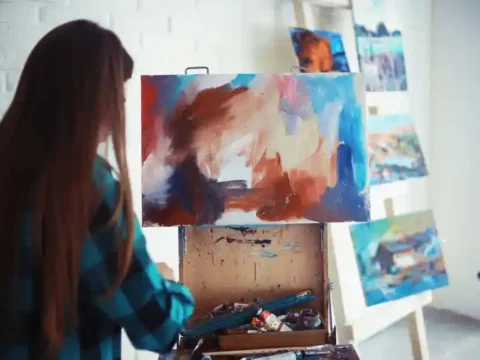 College student painting on a canvas in an art studio, illustrating how hobbies and social activities support student life and personal growth.
