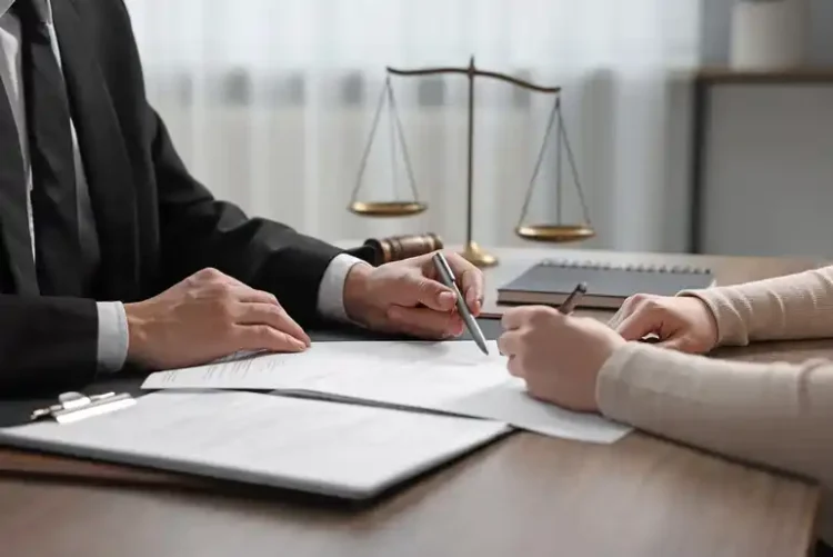 Inside a Modern Divorce Practice: How Firms Like MM Law Approach Client-Centered Representation A lawyer in a black suit pointing at legal documents while consulting with a client at a desk, featuring a scale of justice in the background.