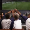 The Pint Is No Longer the Whole Night Friends raising beer glasses while watching a soccer match together at a lively bar, highlighting the social experience beyond the pint.