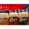 A poster for an anniversary event at obec brewing with three pints of beer in various shades
