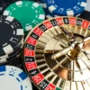 5 Mistakes to Avoid When Playing Live Roulette Online for the First Time Miniature gold roulette wheel resting on a laptop keyboard next to stacks of casino poker chips, representing online live roulette play.