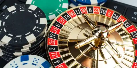 Miniature gold roulette wheel resting on a laptop keyboard next to stacks of casino poker chips, representing online live roulette play.