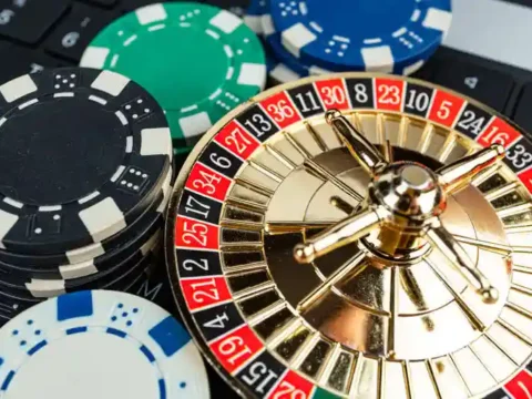 5 Mistakes to Avoid When Playing Live Roulette Online for the First Time Miniature gold roulette wheel resting on a laptop keyboard next to stacks of casino poker chips, representing online live roulette play.