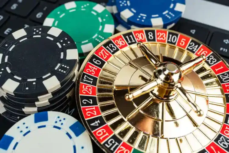 5 Mistakes to Avoid When Playing Live Roulette Online for the First Time Miniature gold roulette wheel resting on a laptop keyboard next to stacks of casino poker chips, representing online live roulette play.