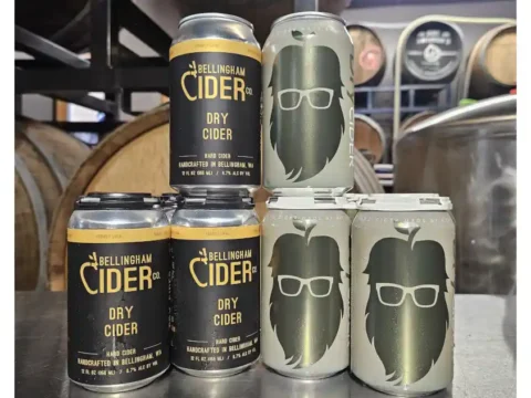 Cans of cider from stacked up with barrels in the background
