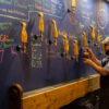 The Washington Bottle-Share Playbook: Small Pours, Local Stories and a Table Game Between Flights A taproom with a cozy interior, featuring a bartender standing in front of a blue board.