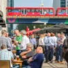 The Walkable Brewery Neighborhood: What It Costs to Live Near Seattle’s Taproom Clusters People enjoying drinks at a Seattle brewery neighborhood with a city transit bus overhead.